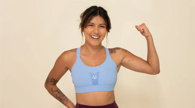 Gril flexing her bicep while smiling and wearing a cornflower blue Maaree Solidarity sports bra