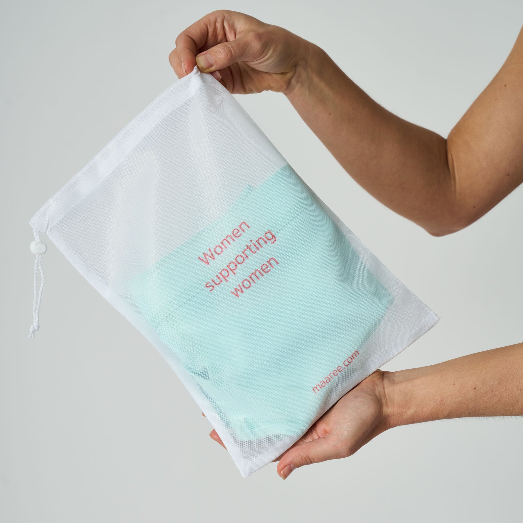 Light blue wash bag with 'Woman Supporting Women' text in a white drawstring bag on a light gray background