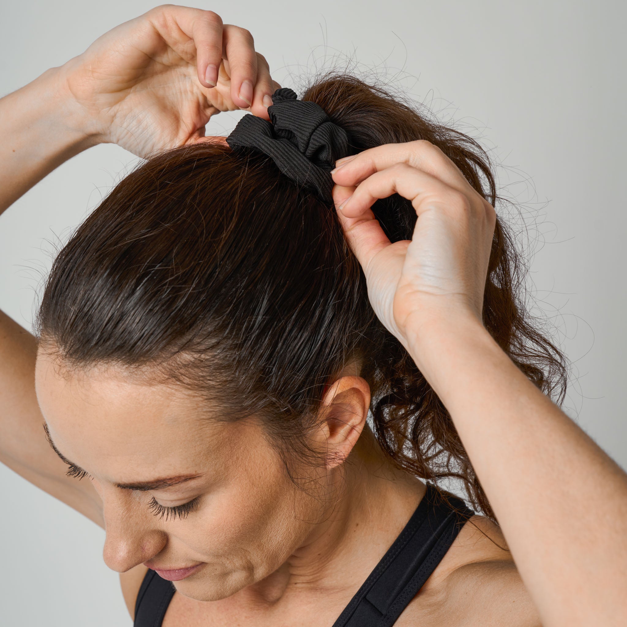 Woman adjusting a black scrunchie in her hair against a neutral background
