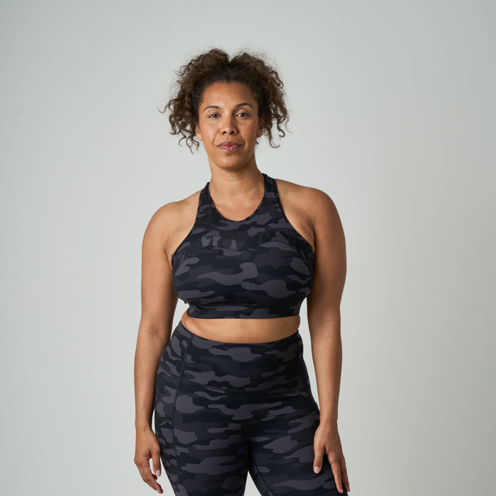 Woman wearing a black camouflage sports bra and leggings on a gray background