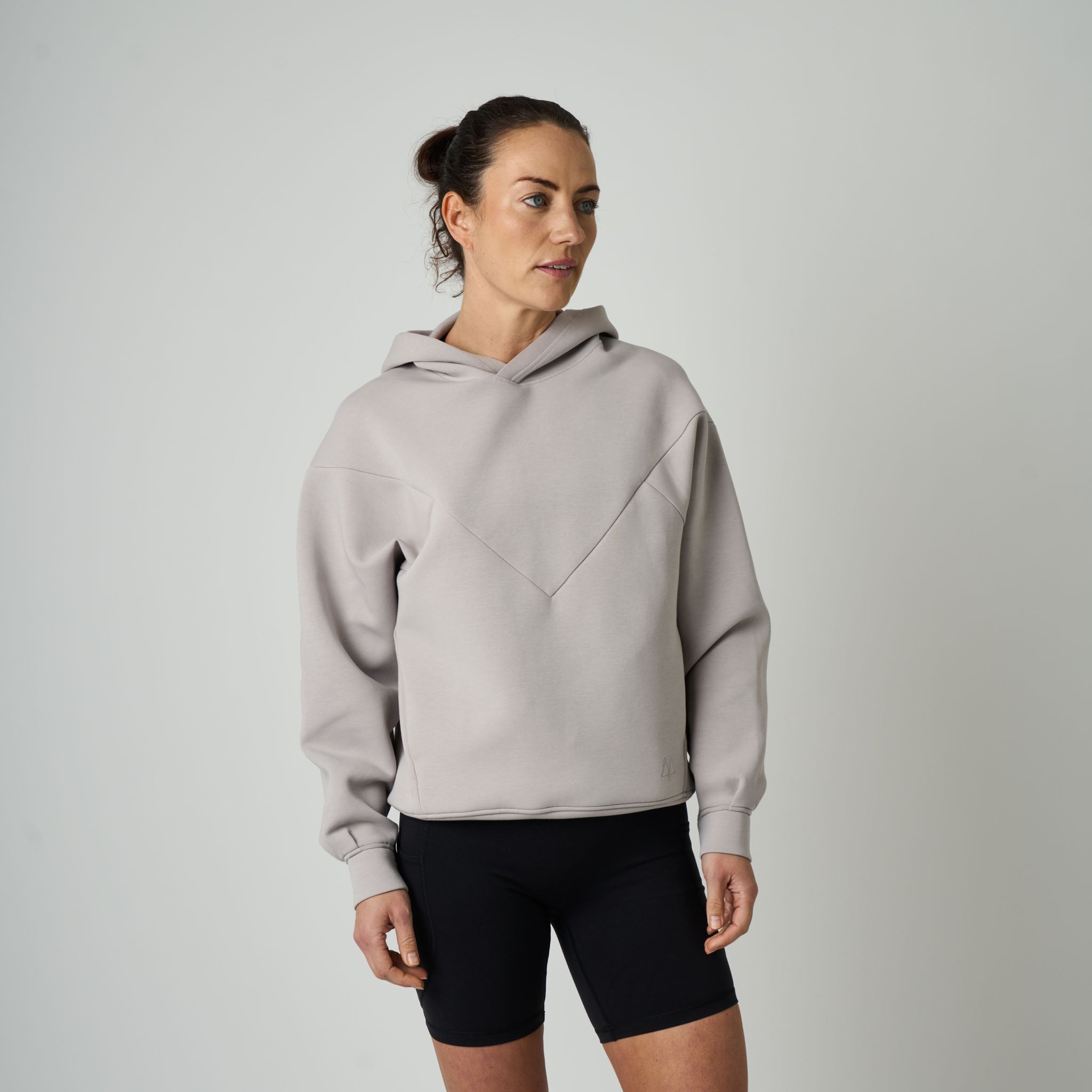 Woman wearing a light gray hoodie and black shorts on a plain background