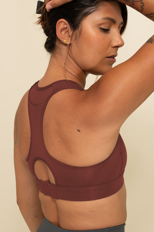 Woman in Burgundy high-support sports bra facing backwards, showing the rear pocket and hook and eye clasp.